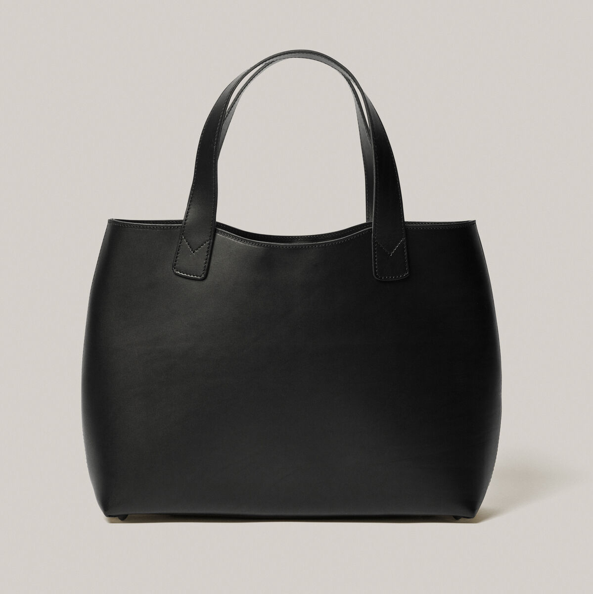 Eine elegante schwarze Tasche aus Kernleder mit zwei Griffen. Die Tasche hat ein minimalistisches und zeitloses Design.