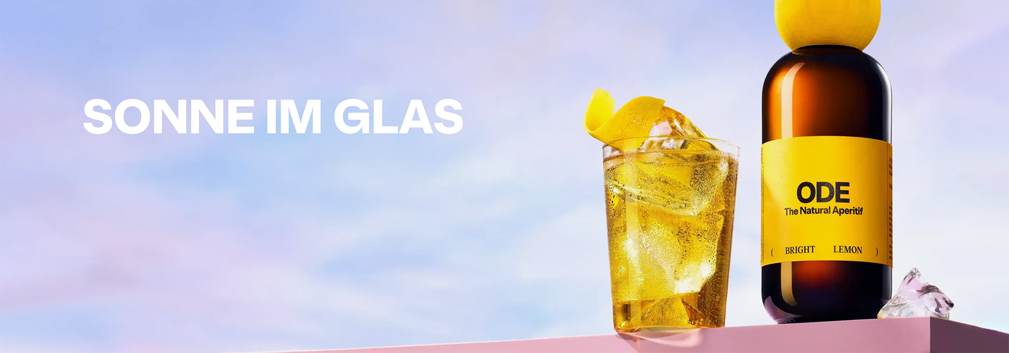 Flasche ODE Aperitif mit Zitrone und Glas mit Eiswürfeln vor blauem Himmel, Text 'SONNE IM GLAS'