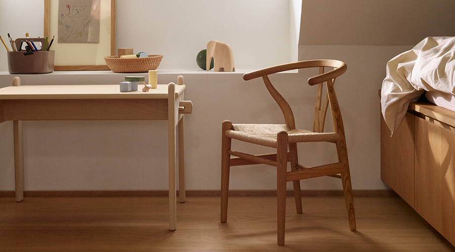 Moderner Holzstuhl mit geflochtenem Sitz neben einem hellen Schreibtisch mit Stiftebehälter und Dekoration in einem minimalistisch eingerichteten Raum