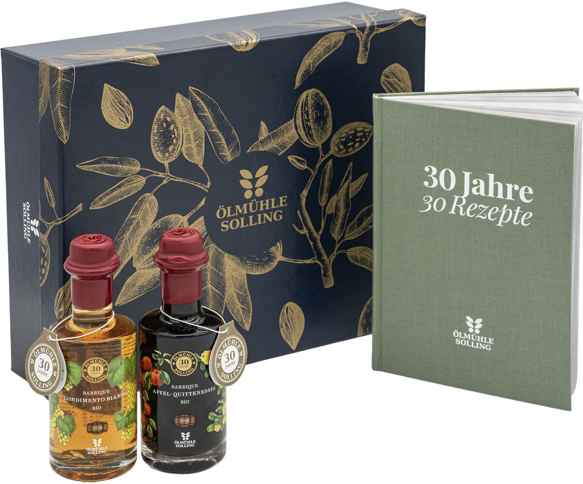 Die ZEIT Präsentbox Jubiläumsessige der Ölmühle Solling enthält zwei Flaschen Jubiläumsessig mit festlichen Etiketten und ein grünes Rezeptbuch "30 Jahre – 30 Rezepte". Die edle Geschenkbox ist dunkelblau mit goldenen Pflanzenmotiven verziert, Bio- und Sonderedition-Label sichtbar.