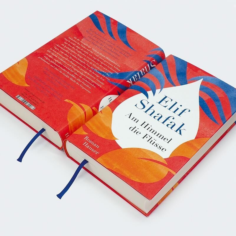 Das Bild zeigt das Buch 'Am Himmel die Flüsse' von Elif Shafak. Es hat einen roten Einband mit blauen und orangefarbenen Motiven sowie einem weißen Titelbereich. Zwei Bücher liegen nebeneinander, eines ist geöffnet und zeigt ein Lesezeichen.