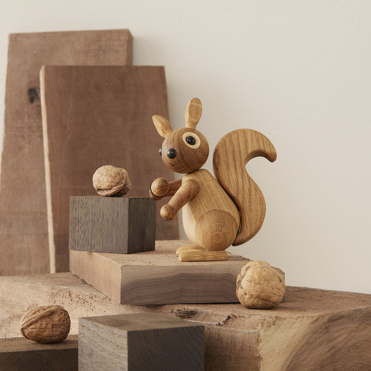 Holzfigur eines Eichhörnchens mit beweglichen Armen und Schwanz, auf mehreren unterschiedlich großen und farbigen Holzklötzen arrangiert, umgeben von Walnüssen auf einer natürlichen Holzoberfläche.