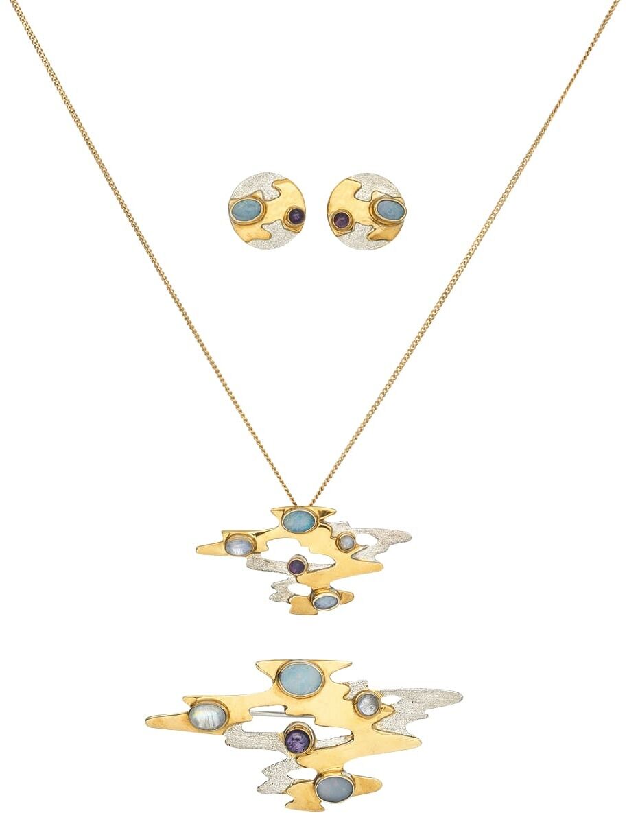 Eine elegante Brosche namens »Monet Reflections«, die ein kunstvolles und abstraktes Design aufweist. Sie besteht aus goldenen und silbernen Farbtönen, verziert mit blauen, violetten und weißen Details.