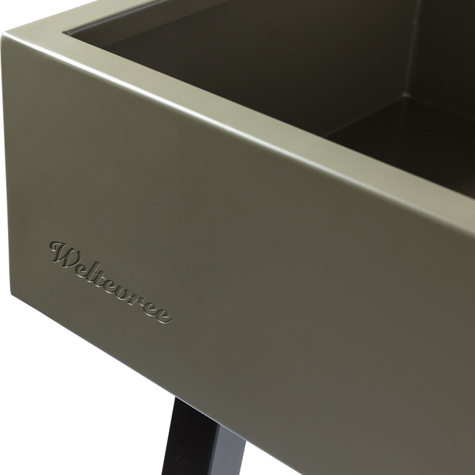 Der Bildausschnitt zeigt eine Ecke des grünen Pflanztischs »Gardenworks Station« der Marke Weltevree. Die Außenfläche ist glatt und modern, das Markenlogo ist dezent auf der Seitenwand eingraviert. Ein schwarzes Tischbein ist am unteren Rand sichtbar.