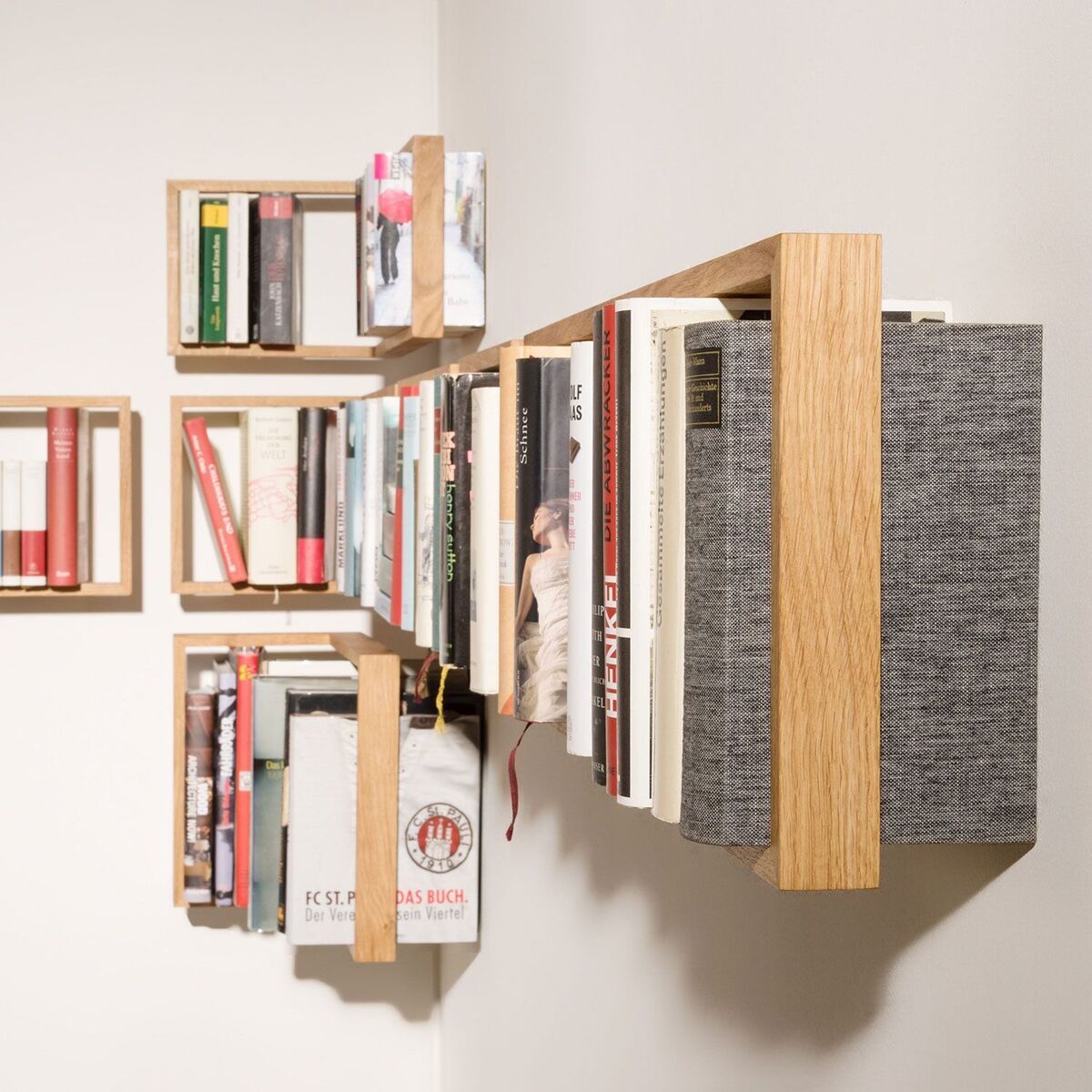 An der Wand montiertes Bücherregal aus Holz mit mehreren Büchern in verschiedenen Farben. Das Regal hat ein minimalistisches Design und bietet eine moderne Aufbewahrungslösung für Bücher.