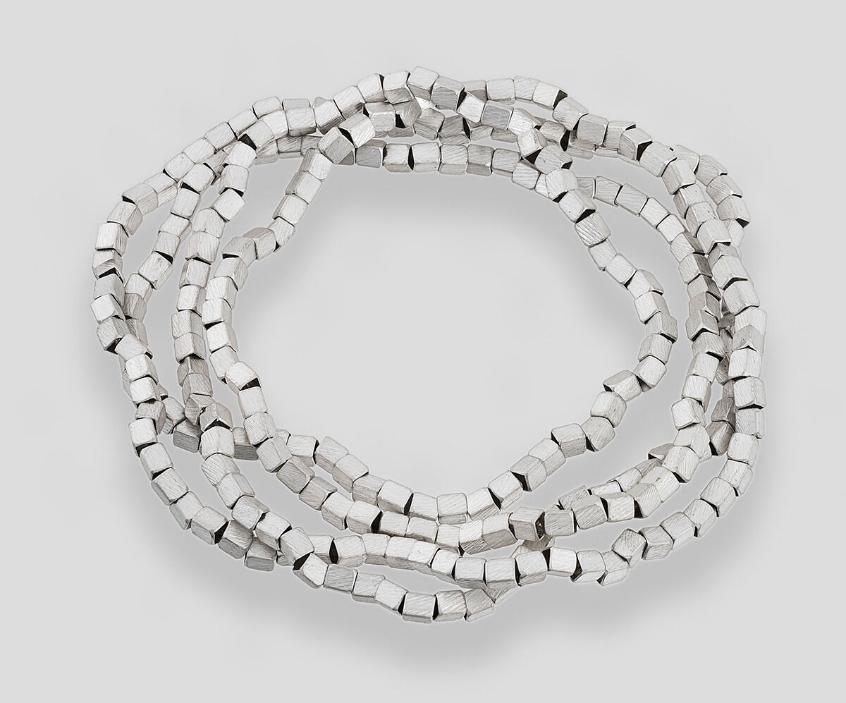 Eine schlichte silberne Kette mit würfelförmigen Perlen, die auf einem neutralen Hintergrund angeordnet ist.