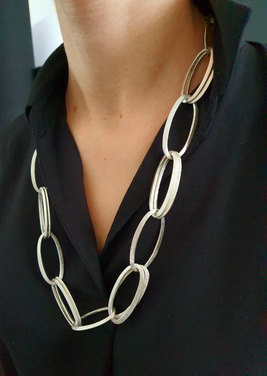 Jemand trägt eine silberne Halskette mit ovalen Gliedern über einer schwarzen Bluse.