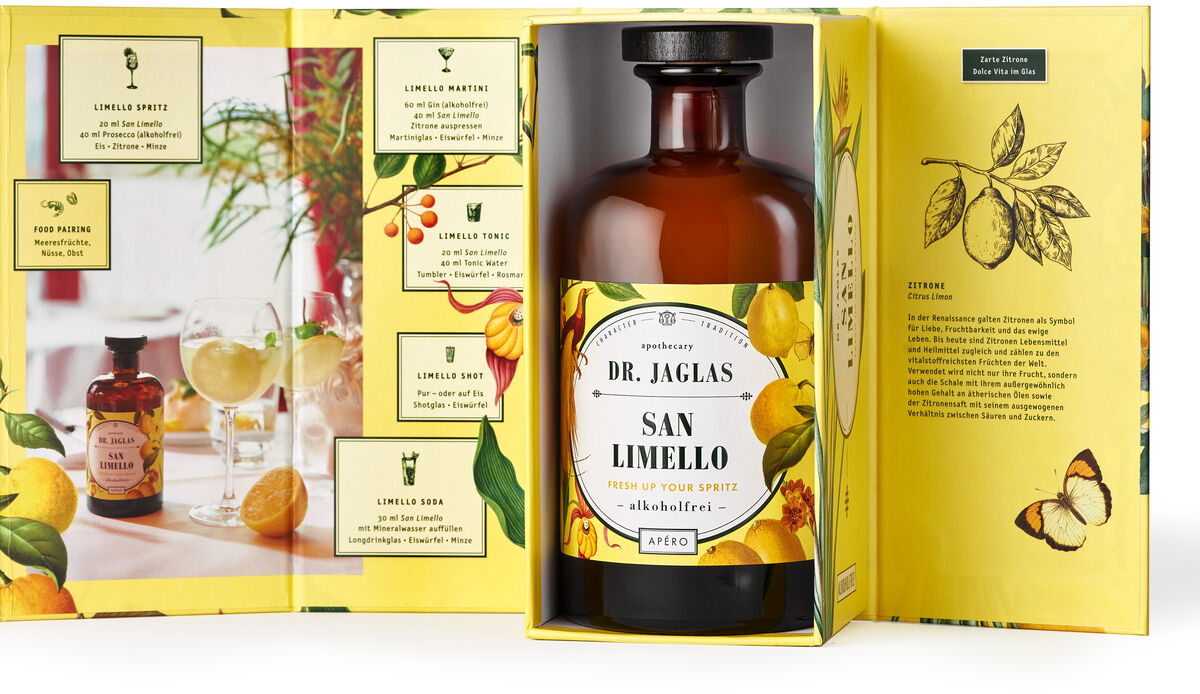 Eine Flasche des alkoholfreien Aperitifs »San Limello« von Dr. Jaglas ist in einer gelben Geschenkverpackung mit Zitronenmotiven präsentiert. Die Verpackung ist geöffnet und zeigt Text und Illustrationen zu dem Produkt.