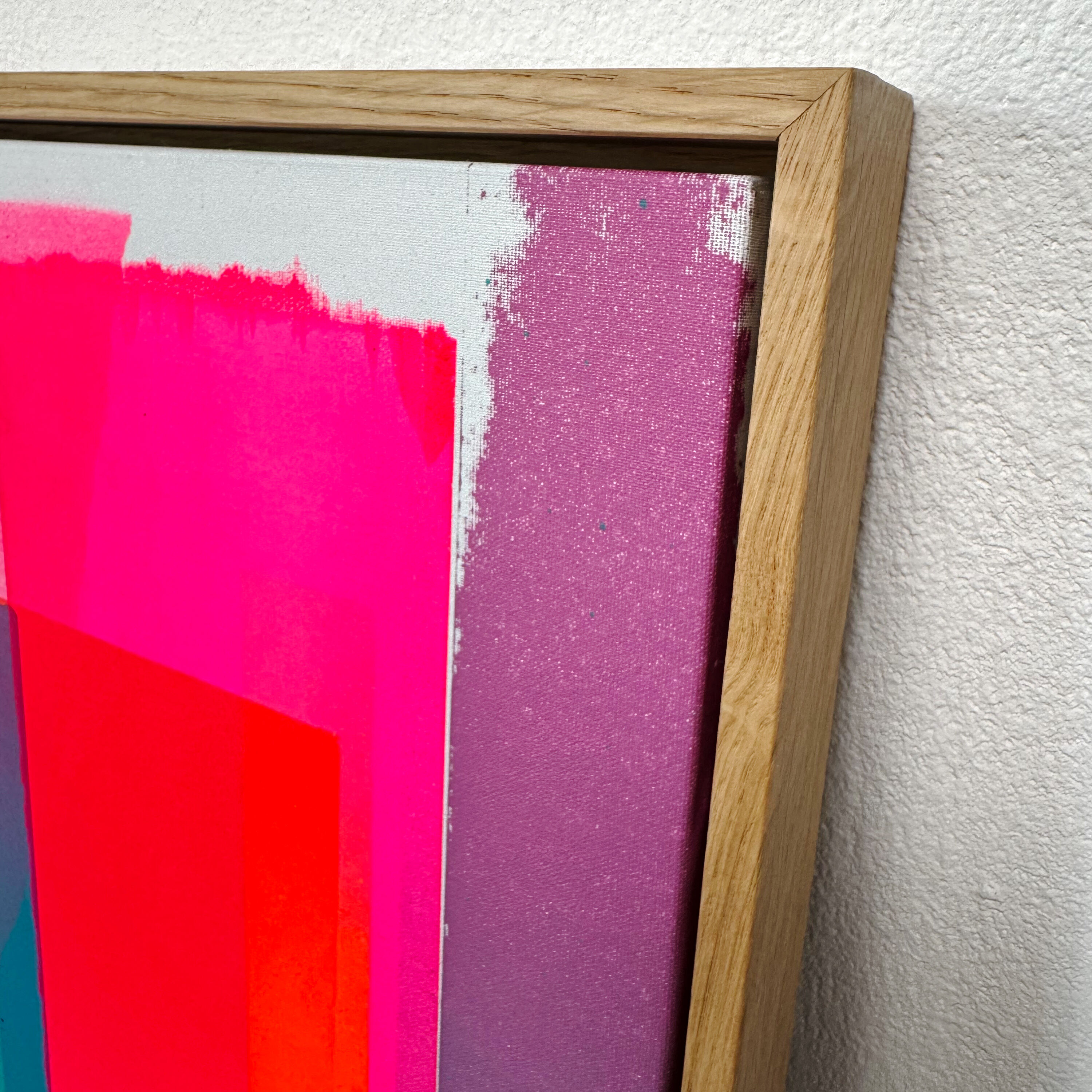 Detailaufnahme eines modernen Siebdrucks „Gratitude - No.2“, der in leuchtenden Pink- und Lilatönen gearbeitet und in einem naturfarbenen Holzrahmen gerahmt ist. Das Kunstwerk zeigt abstrakte Farbflächen und eignet sich besonders als farbenfrohe Wanddekoration für zeitgenössisch eingerichtete Räume.