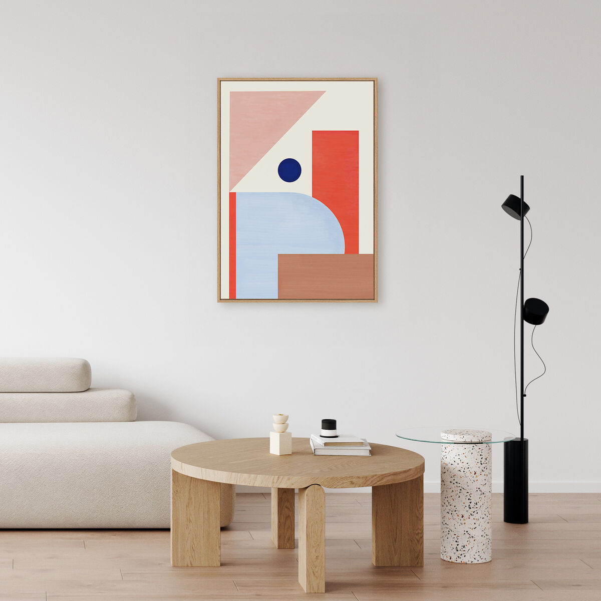 Abstraktes Leinwandbild in geometrischem Stil an einer weißen Wand über einem minimalistischen beigen Sofa und einem runden Holztisch, mit modernen Dekorationselementen in einem hell eingerichteten Wohnzimmer.