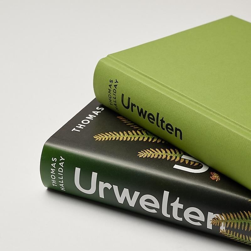 Zwei Bücher von Thomas Halliday mit dem Titel 'Urwelten' liegen übereinander. Das obere Buch hat einen grünen Umschlag, und das untere Buch hat einen schwarzen Umschlag mit einem goldenen Farnblatt.