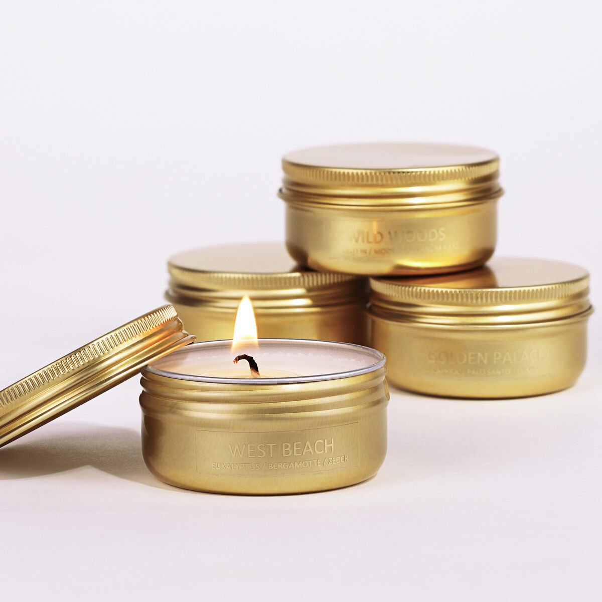 Eine Sammlung von fünf goldenen Reiseduftkerzen in kleinen Dosen, eine davon brennend.