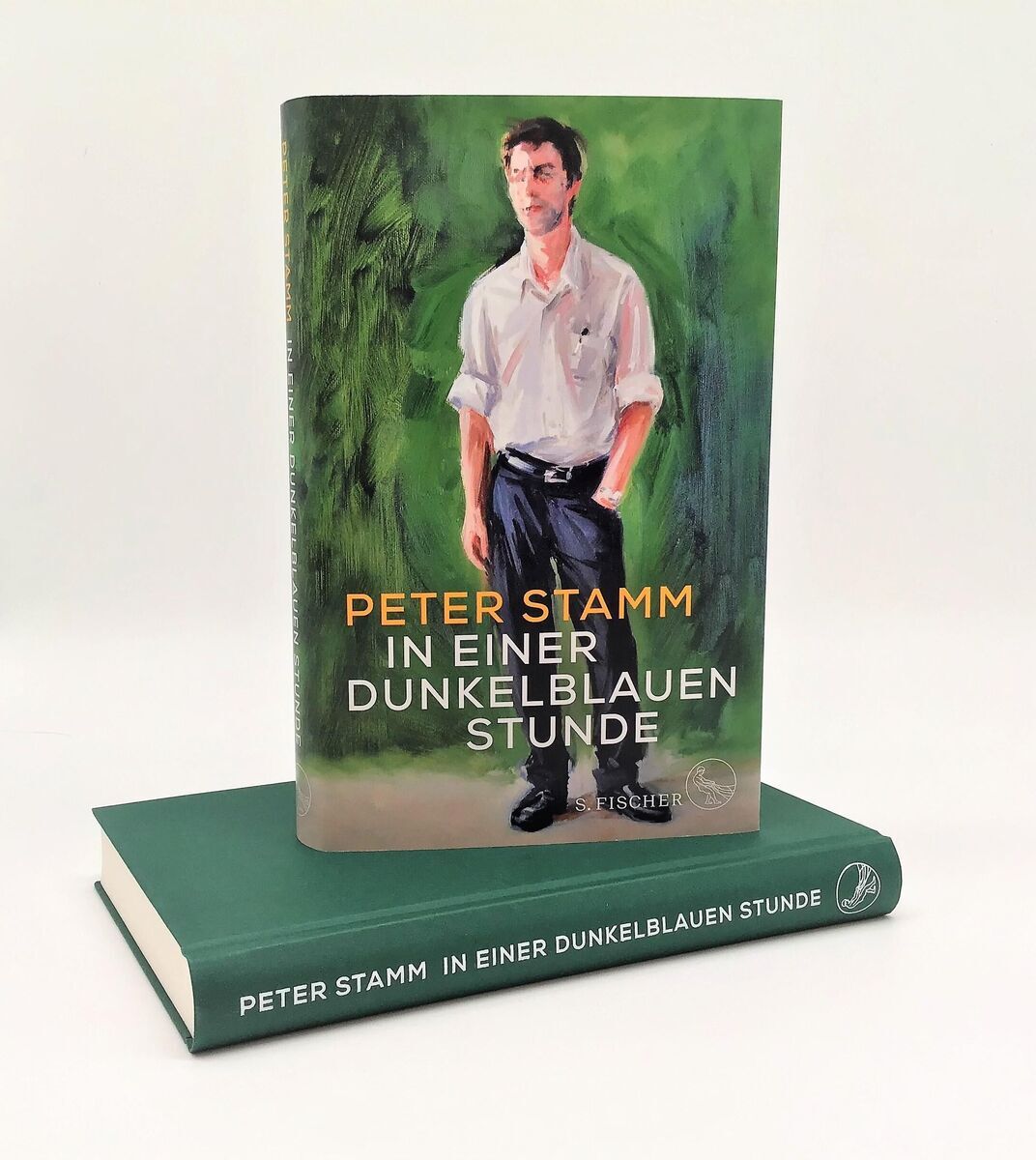 Das Bild zeigt das Buch 'In einer dunkelblauen Stunde' von Peter Stamm. Das Cover des Buches zeigt eine Illustration eines Mannes in einem weißen Hemd und dunkler Hose vor einem abstrakten grünen Hintergrund. Der Titel und der Name des Autors sind in orangefarbenen Buchstaben geschrieben. Das Buch steht auf einem weiteren Buch mit demselben Titel, dessen Einband dunkelblau ist.