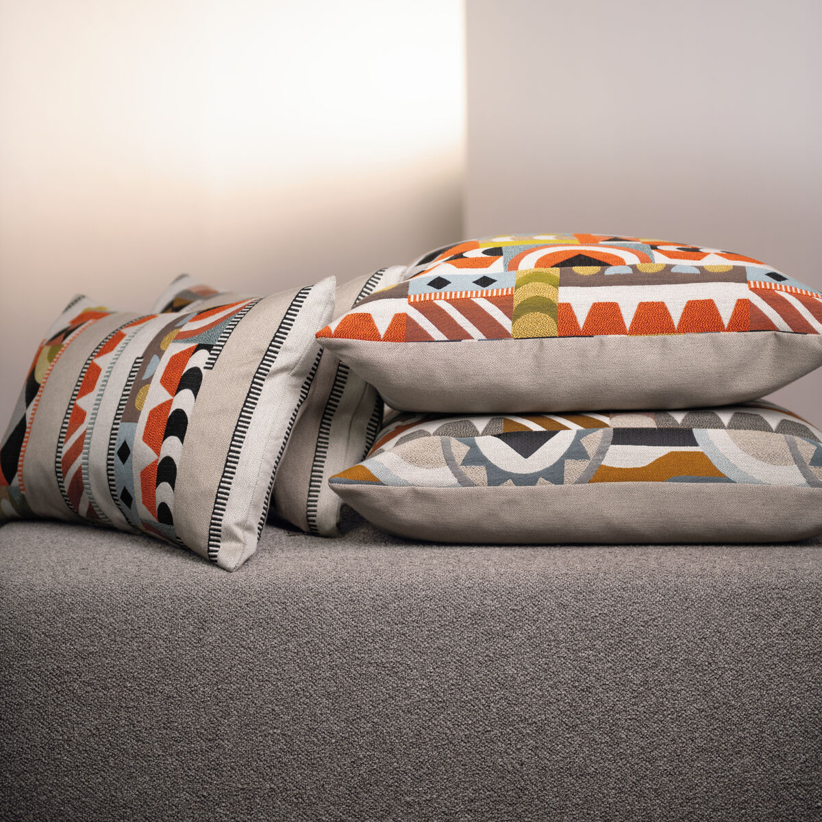 Mehrere dekorative Kissen mit geometrischen und bunten Mustern auf einem grauen Sofa ausgestellt.