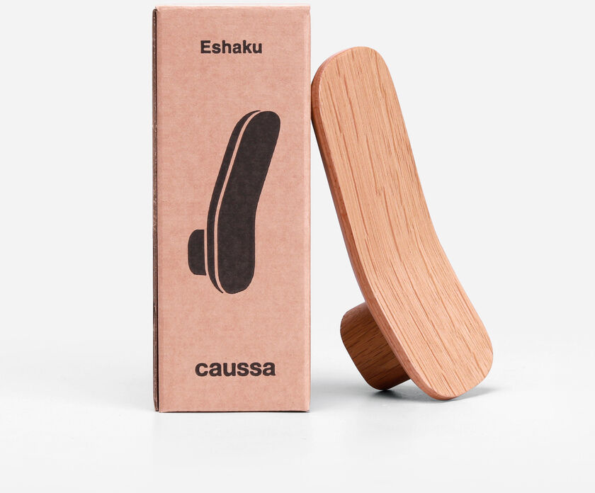 Kleiderhaken »Eshaku« aus Eiche, gezeigt vor seiner rechteckigen Verpackung aus braunem Karton. Das Design ist modern und minimalistisch mit einer natürlichen Holzoptik.