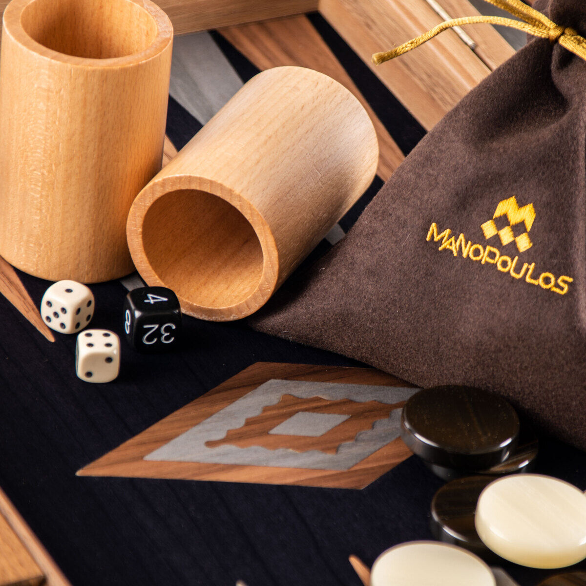 Backgammon-Spielbrett aus Schwarzeiche mit Walnussintarsien, zwei Holzbecher, diverse Spielsteine und Würfel, mit Manopoulos-Logo auf einer Stofftasche.