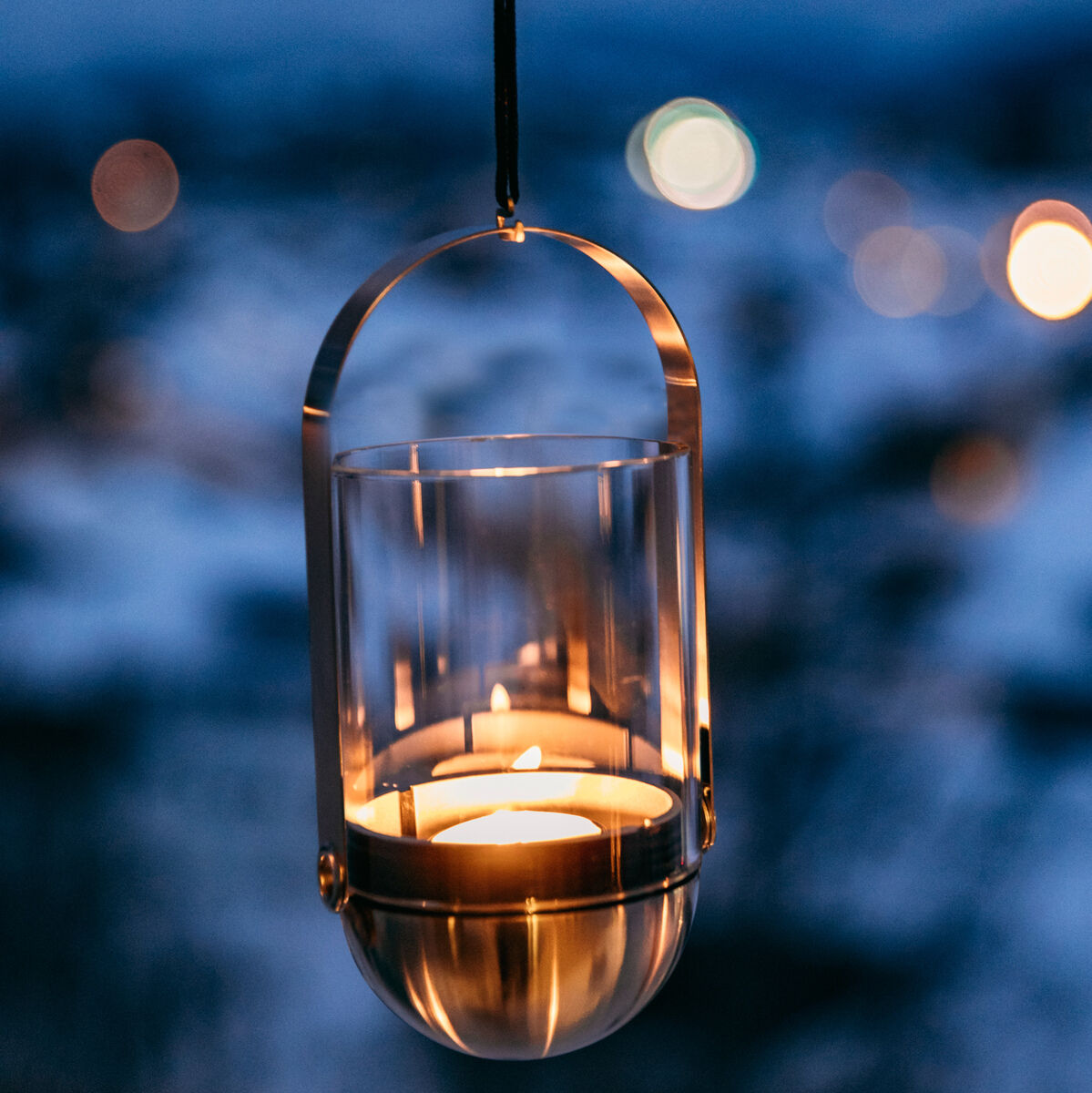 Eine gravitationskerze, die in einem Glas- und Metallgehäuse hängt und im Hintergrund eine verschwommene Leuchtlandschaft in Blau- und Weißtönen zeigt.