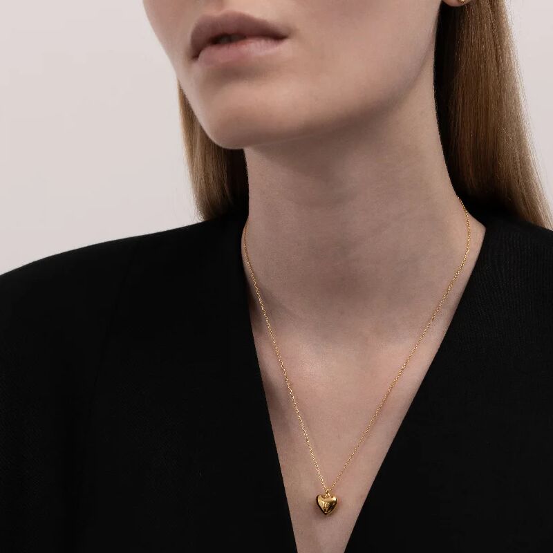 Eine Frau trägt ein elegantes Collier mit herzförmigem Anhänger aus Gold. Die feine Goldkette und das schlichte Design ergänzen ein schwarzes Oberteil. Das Schmuckstück wirkt modern und geschmackvoll und eignet sich besonders als Geschenk zu festlichen Anlässen.