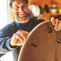 Eine Person hält ein Sensoboard aus Holz in einer Werkstatt. Das Sensoboard hat eine runde Form mit mehreren Griffen.