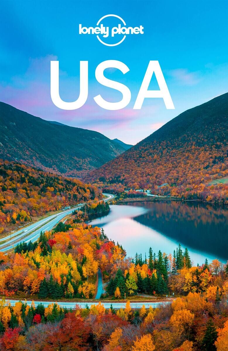 Das Buchcover des 'Lonely Planet Reiseführer USA' zeigt eine atemberaubende Herbstlandschaft mit bunten Bäumen, einem ruhigen See und einer Straße, die zwischen zwei Bergen verläuft. Oben steht das Logo von Lonely Planet und das Wort 'USA' in weißer Schrift.