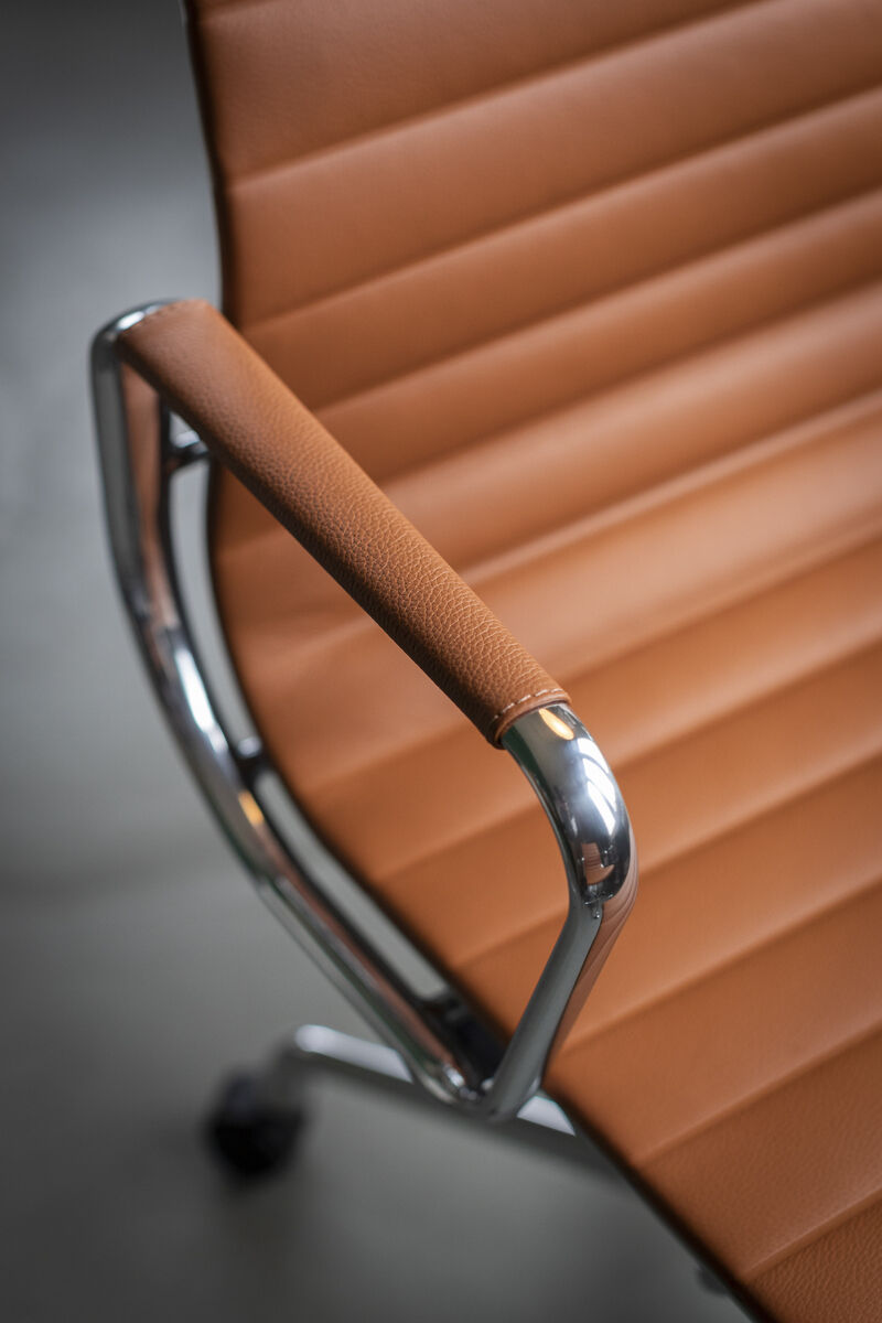 Nahaufnahme eines polierten Vitra Alu Chair EA 118. Der Stuhl hat eine braune Lederpolsterung und glänzende Metallarmlehnen. Das Design ist modern und minimalistisch.