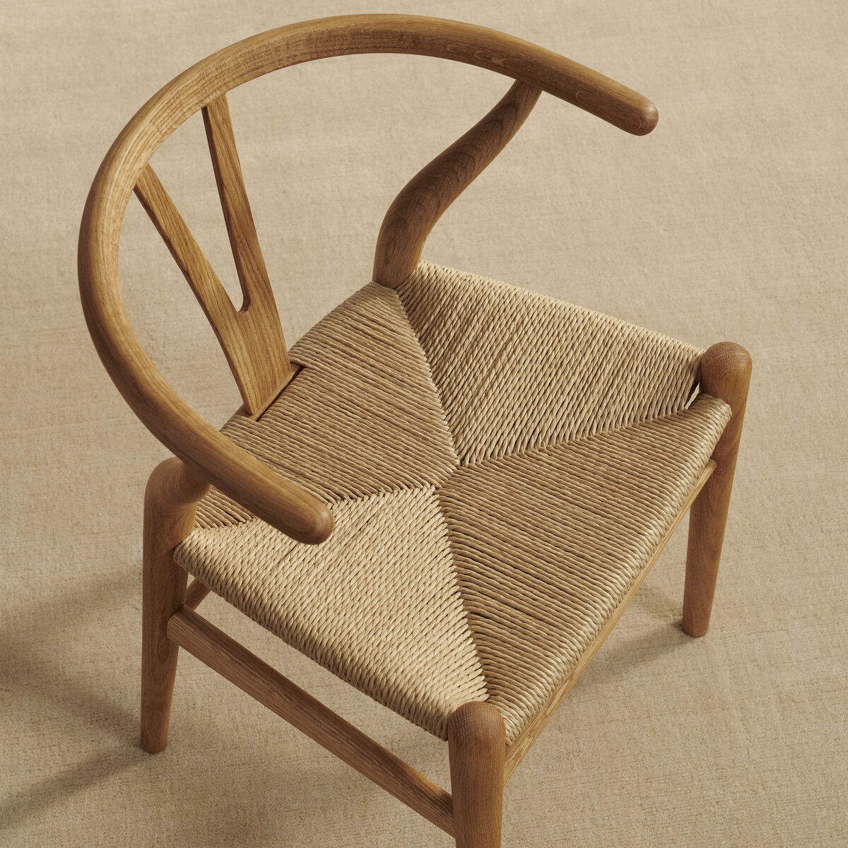 Ein Kindermöbelstück, der Wishbone Chair »CH24 Kinder«, aus Naturholz mit einer skulpturalen Rückenlehne und einem gewebten Leinensitz auf einem beigen Hintergrund.