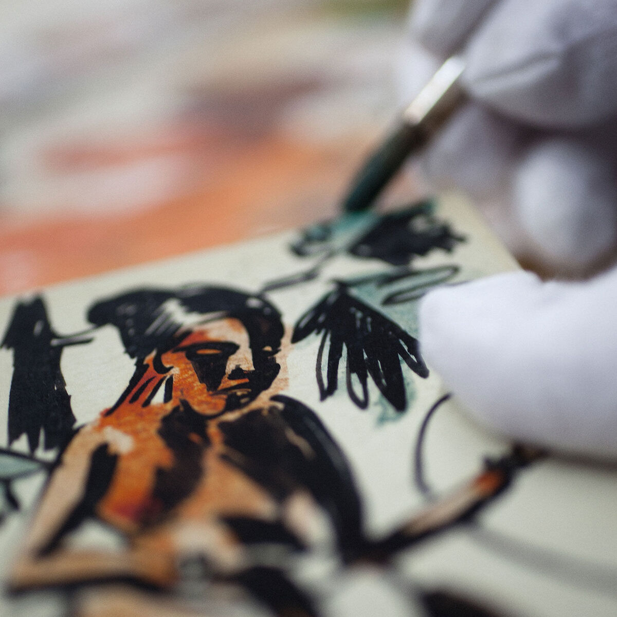 Ein Detailfoto eines handgemalten Miniatur-Kunstwerks von Max Pechstein (1910-1915). Ein behandschuhter Hand hält einen feinen Pinsel und fügt Details zu einem Bild einer sitzenden Frau mit dunklem Haar hinzu. Die Farbpalette umfasst Beige, Schwarz, Rot, Grün und Weiß.