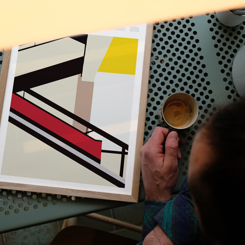 Foto eines eingerahmten Posters mit Bauhaus-Stufenmotiv auf einem perforierten Tisch, daneben eine Espressotasse.