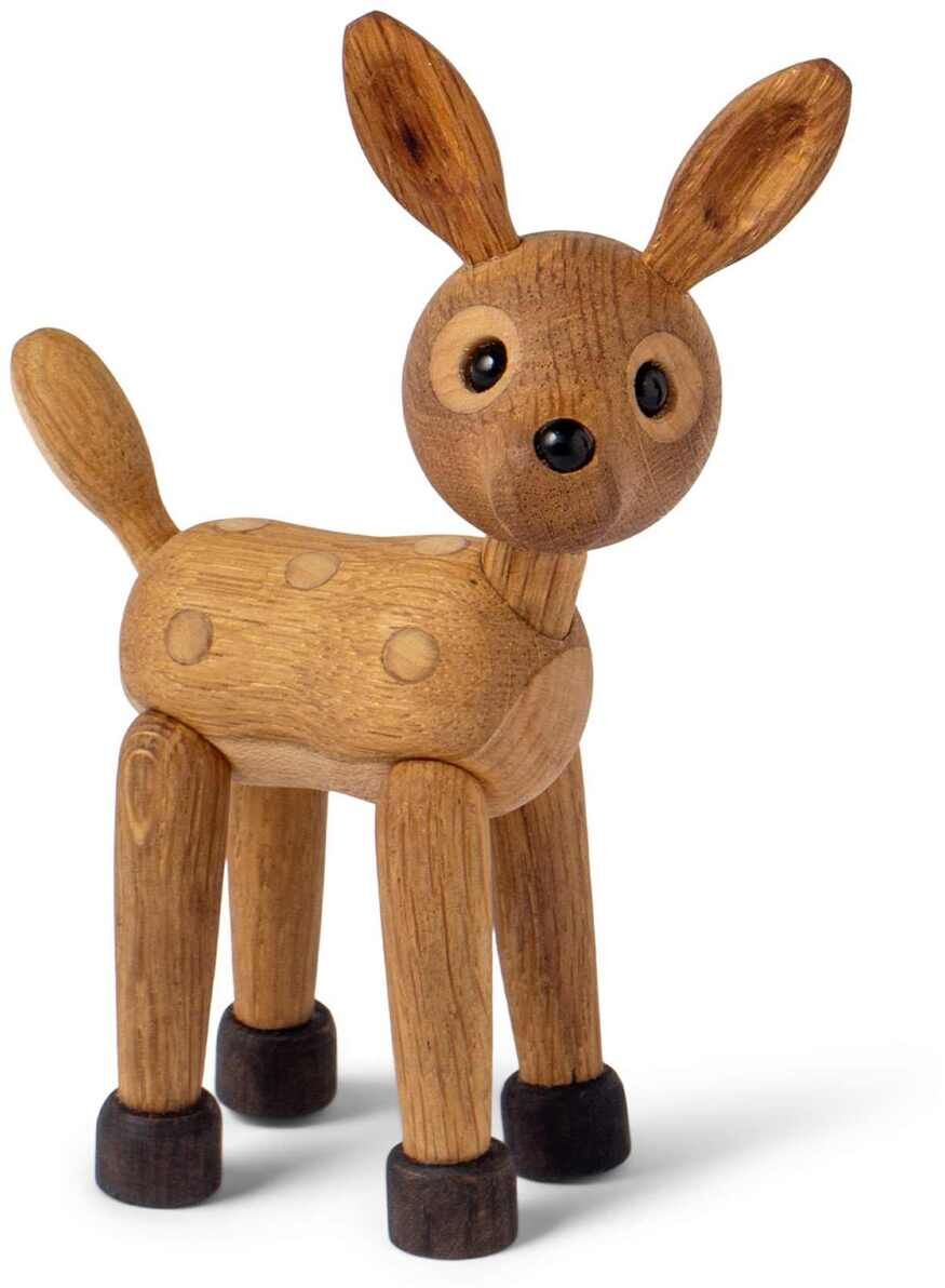 Abgebildet ist eine aus Holz gefertigte Figur eines stehenden Rehkitzes mit runden schwarzen Augen und abstehenden Ohren. Das Design ist schlicht, detailarm und betont natürliche Holzmaserung, teilweise mit dunkleren Akzenten an Ohren, Pfoten und Nase. Die Figur steht frei auf hellem Hintergrund und eignet sich als Dekoration oder Kinderspielzeug.