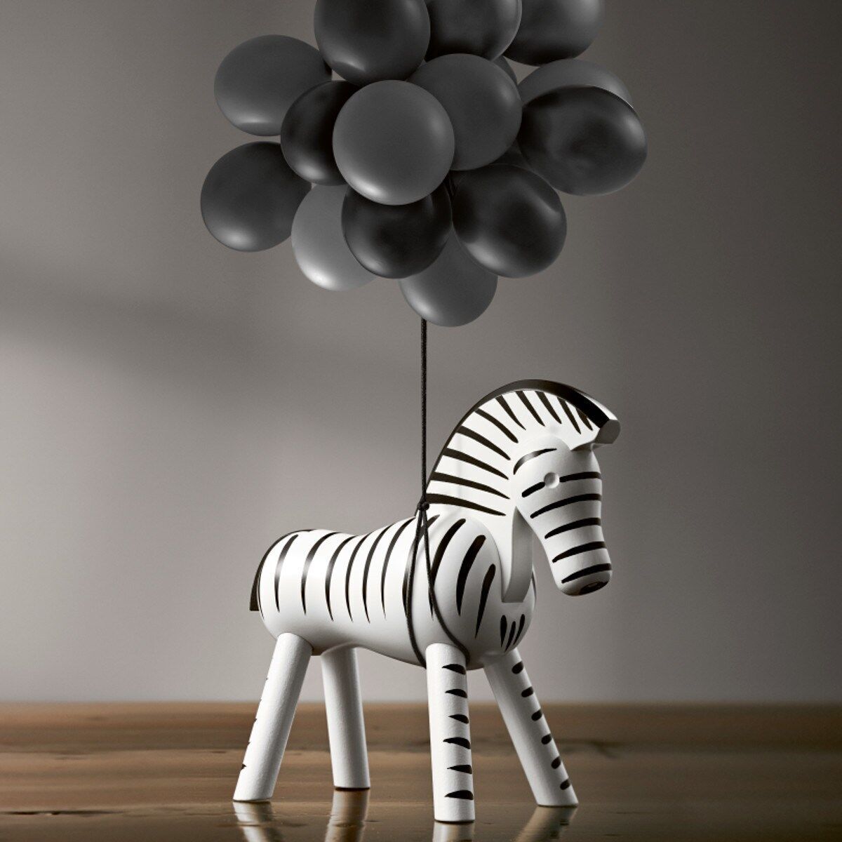 Holzfigur eines Zebras von Kay Bojesen mit schwarz-weißen Streifen steht auf einer Holzoberfläche. Im Hintergrund sind graue Ballons zu sehen.