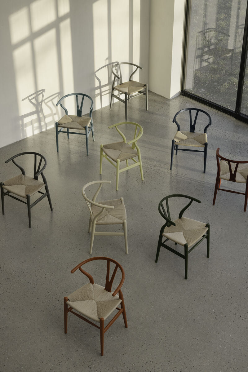 Eine Gruppe von CH24 Soft Stühlen von Carl Hansen in verschiedenen Farben in einem hellen Raum mit Betonboden und großen Fenstern.