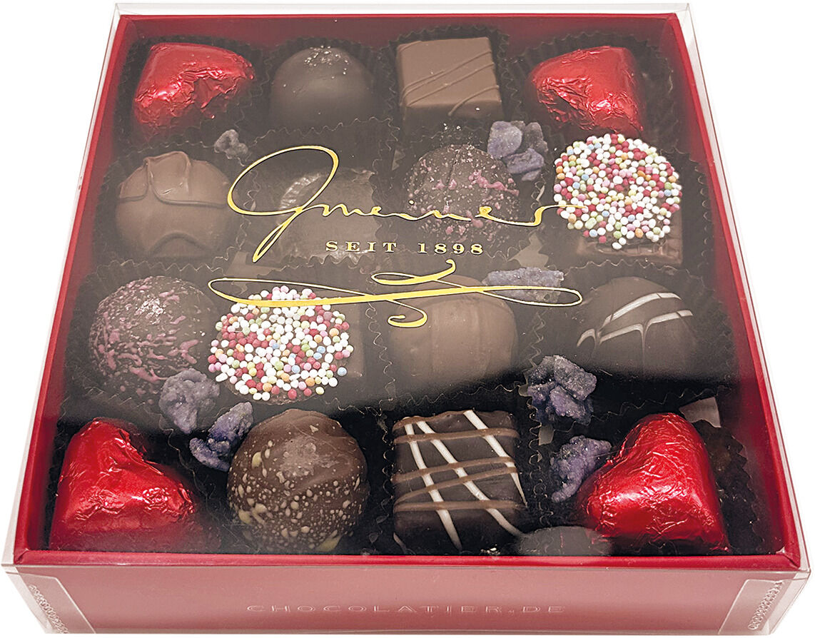 Eine elegante Box mit assortierten Pralinen, darunter rote herzförmige und bunt bestreute Bonbons. Ideal als Geschenk für besondere Anlässe.