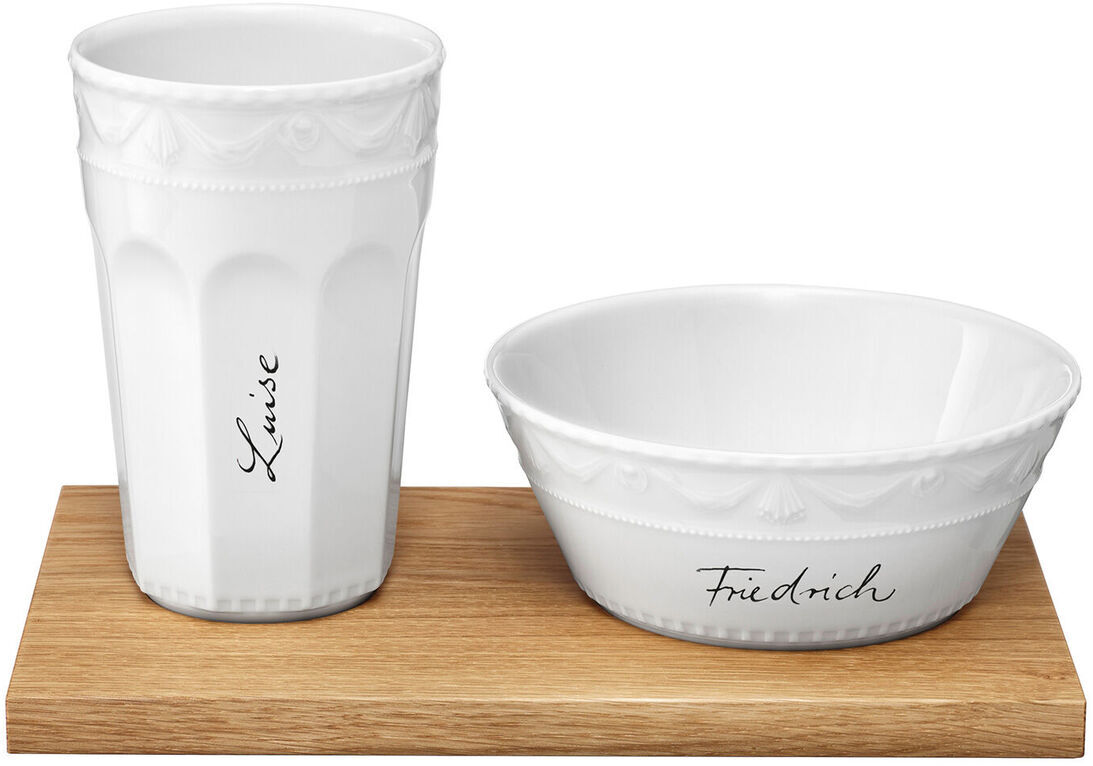 Muesli-Gourmet-Set »Kurland« von KPM, bestehend aus einer weißen Porzellanschale und einem passenden weißen Porzellanbecher mit der kalligraphischen Schriftart Sententia, präsentiert auf einem hellbraunen Holzbrett.