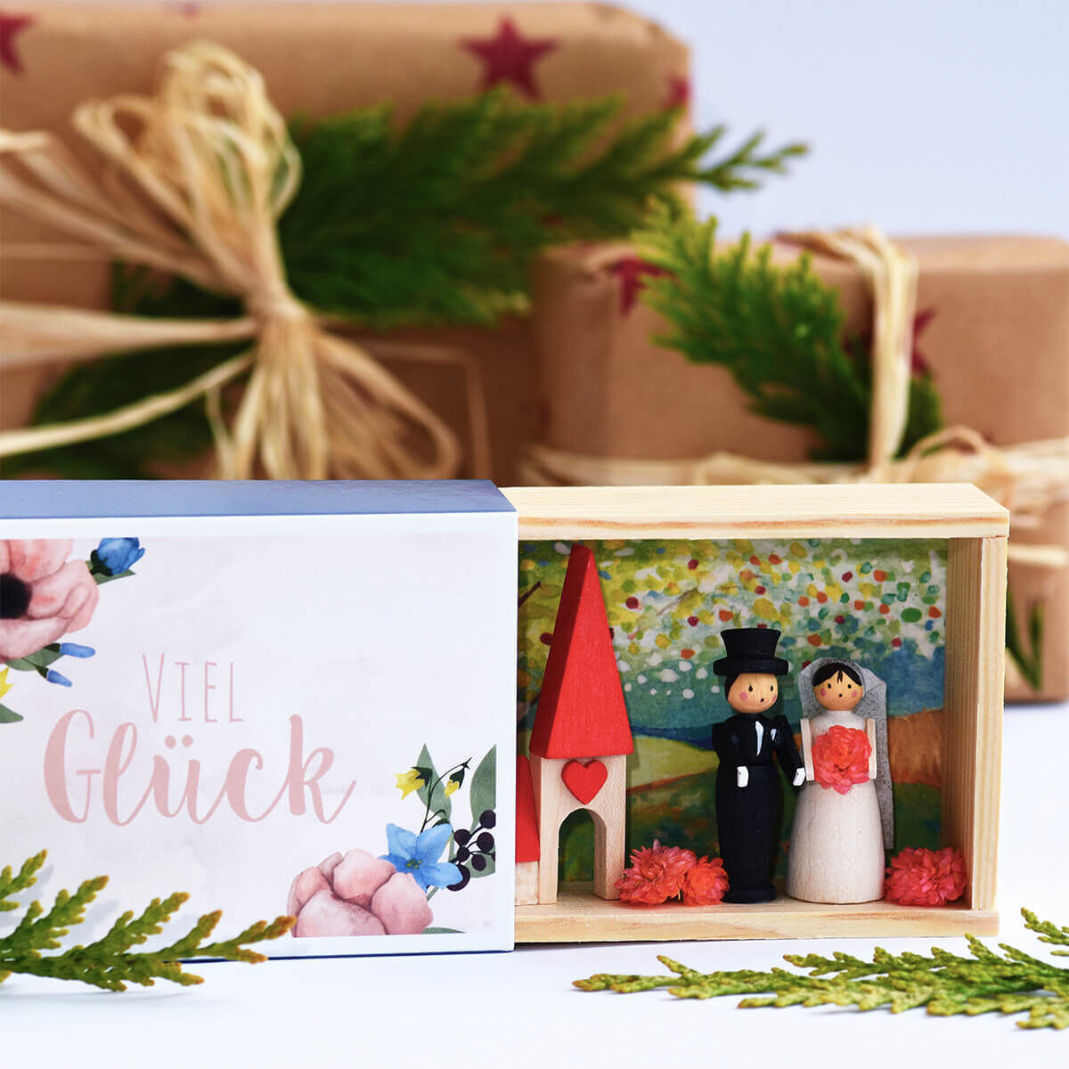Eine handgemachte Glückwunschkästchen mit Brautpaar-Dekoration. Die Box ist aus Holz gefertigt und zeigt ein Brautpaar aus Miniaturfiguren vor einem farbenfrohen Hintergrund in einem kleinen, offenen Häuschen.