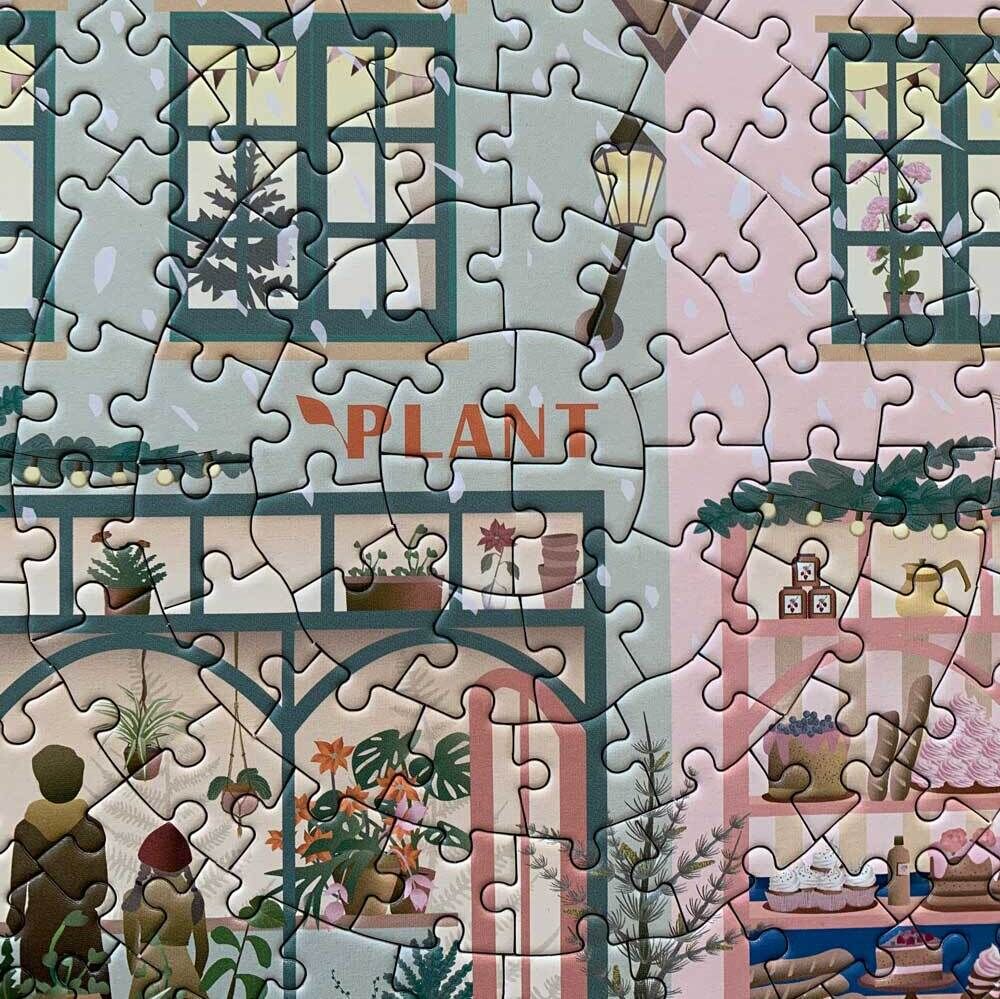 Ein Puzzle mit dem Titel 'Weiße Weihnacht'. Es zeigt ein malerisches Bauernhaus im Winter, geschmückt mit weihnachtlichen Dekorationen. Vor dem Haus befinden sich Pflanzen und Kinder gestalten einen Schneemann. Durch die Fenster sieht man weihnachtlich geschmückte Innenräume.