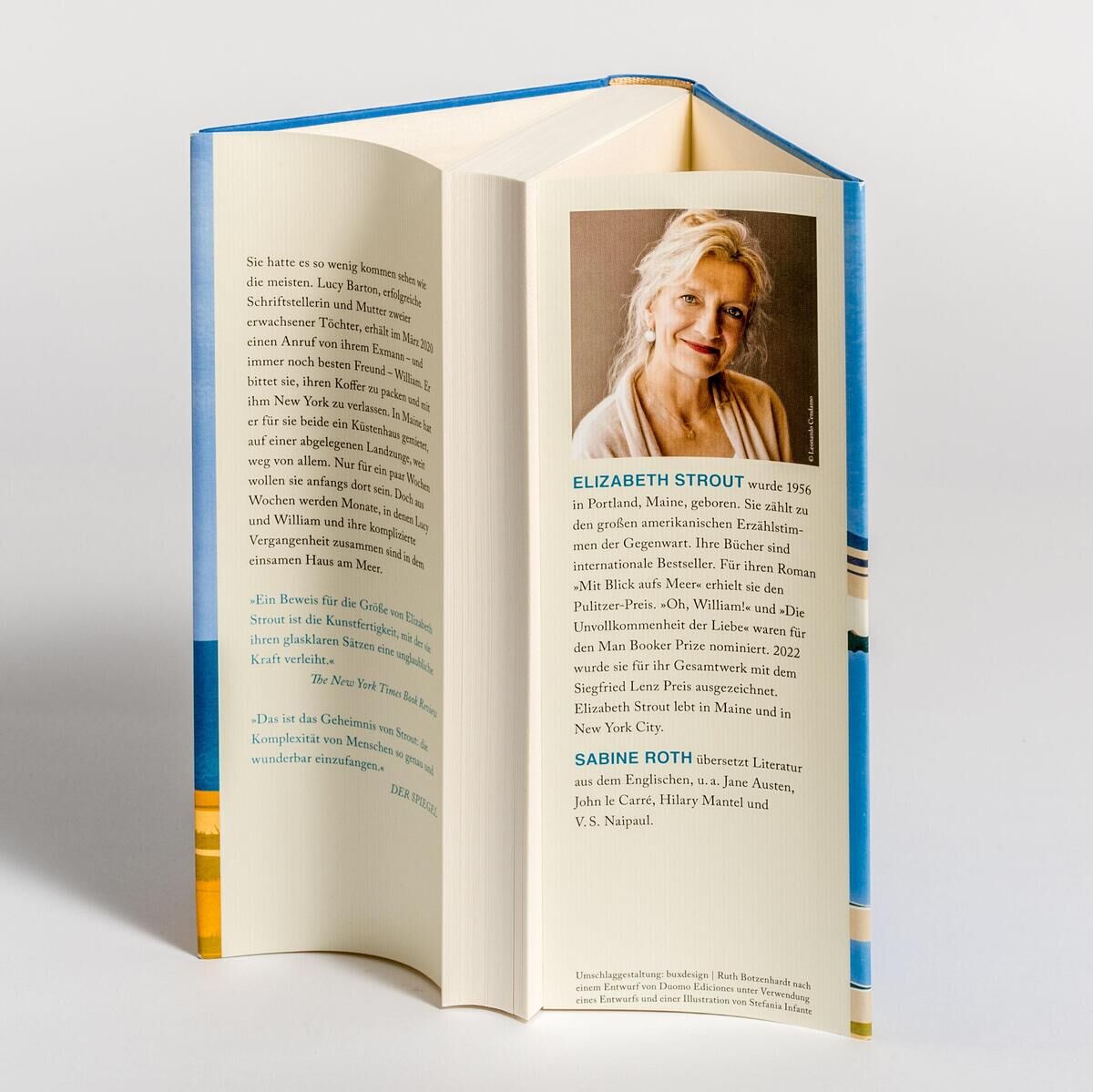 Auf dem Bild ist das Buch 'Am Meer' von Elizabeth Strout zu sehen. Das Buch steht offen, sodass der Buchrücken sowie ein Porträt der Autorin und der Klappentext sichtbar sind. Der Hintergrund ist neutral und das Cover hat hauptsächlich blaue und weiße Farben.
