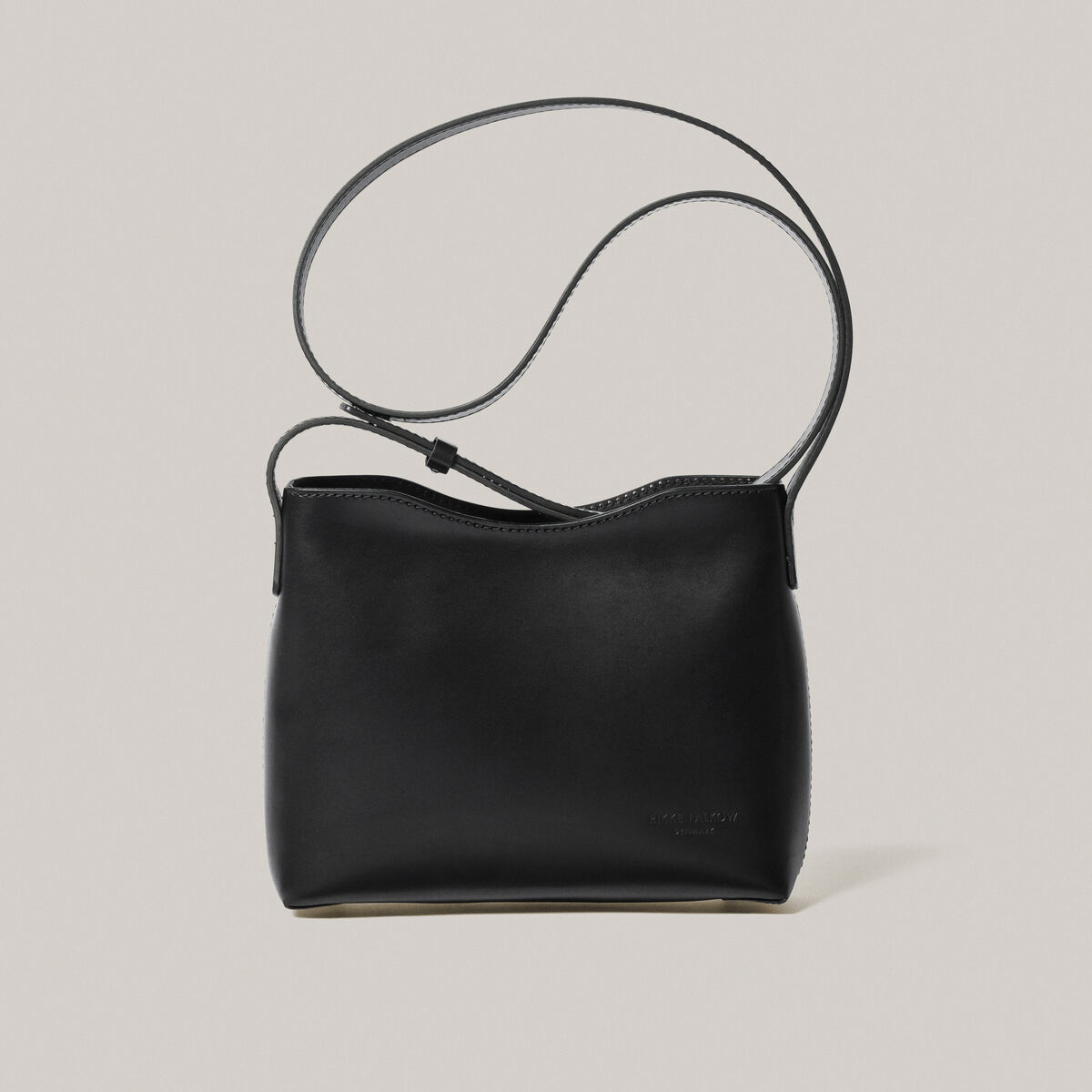 Schwarze Schultertasche aus Kernleder vor einem hellgrauen Hintergrund.