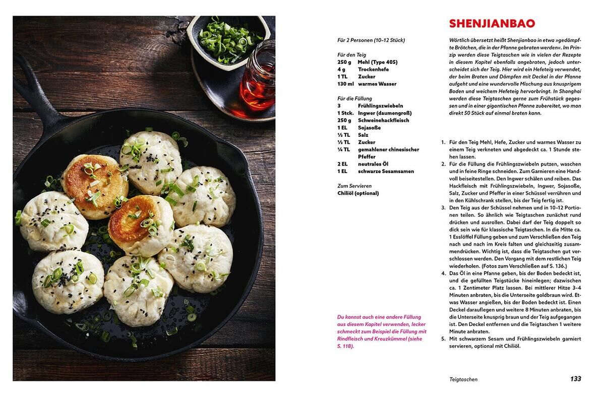 Ein aufgeschlagenes Kochbuch mit dem Titel 'Einfach chinesisch - Rezepte für jeden Tag'. Links im Bild ist eine gusseiserne Pfanne mit mehreren dampfgegarten Brötchen (Shenjianbao), garniert mit Frühlingszwiebeln und Sesamkörnern. Rechts im Bild ist das Rezept für Shenjianbao, samt Zutatenliste und Zubereitungshinweisen, zu sehen. Ein kleiner Behälter mit Sojasauce und ein Schälchen mit geschnittenen Frühlingszwiebeln befinden sich neben der Pfanne.