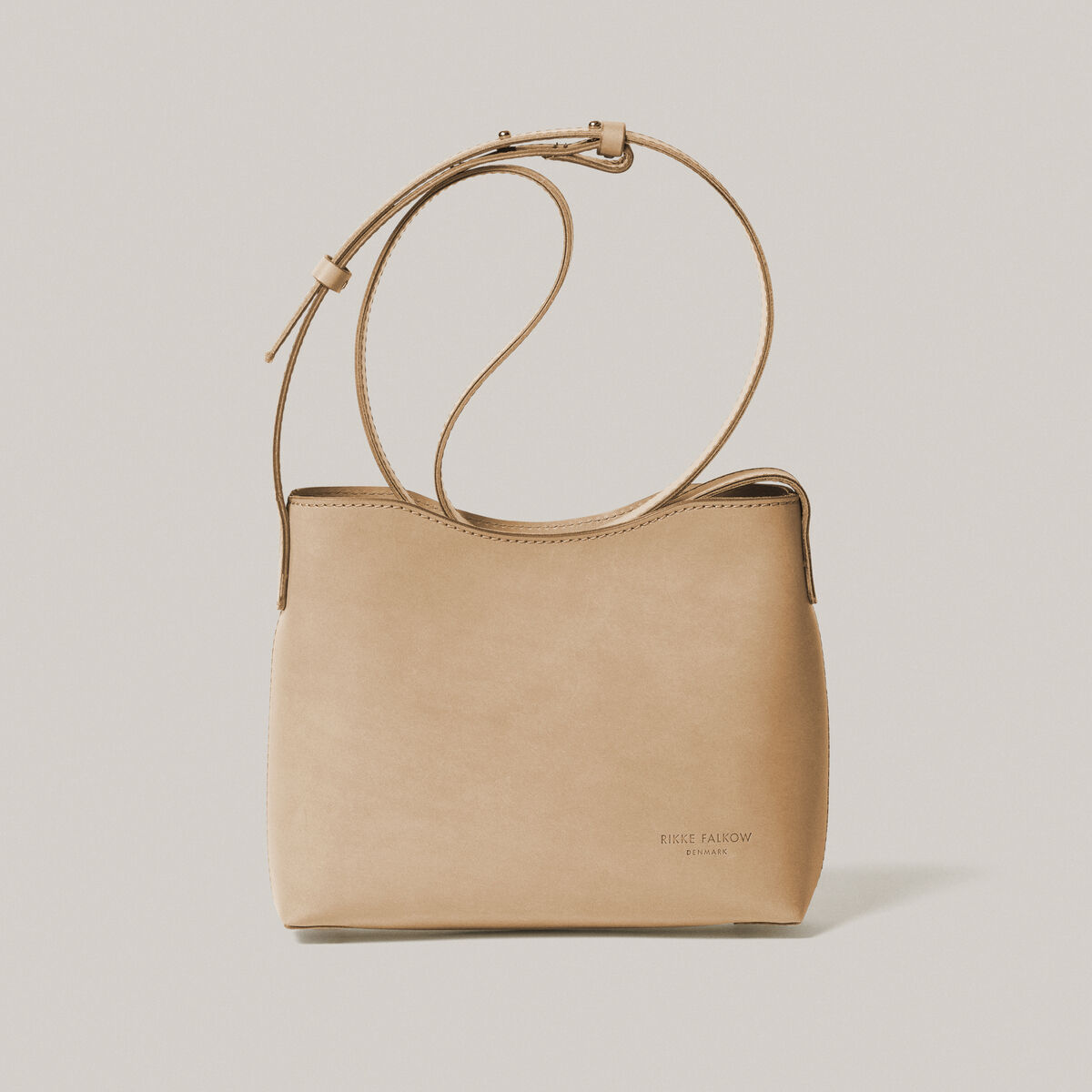 Eine Schultertasche aus hochwertigem, beigem Kernleder mit minimalistischem Design und verstellbarem Schulterriemen auf einem hellen Hintergrund.