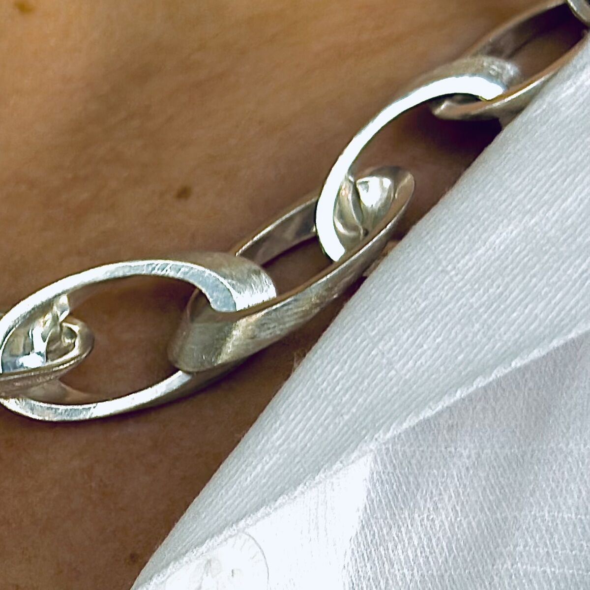 Nahaufnahme eines silbernen Colliers namens "Jackie" um den Hals einer Person, getragen über einem weißen Hemd. Die Kette besteht aus ovalen Gliedern, die elegant und modern wirken.