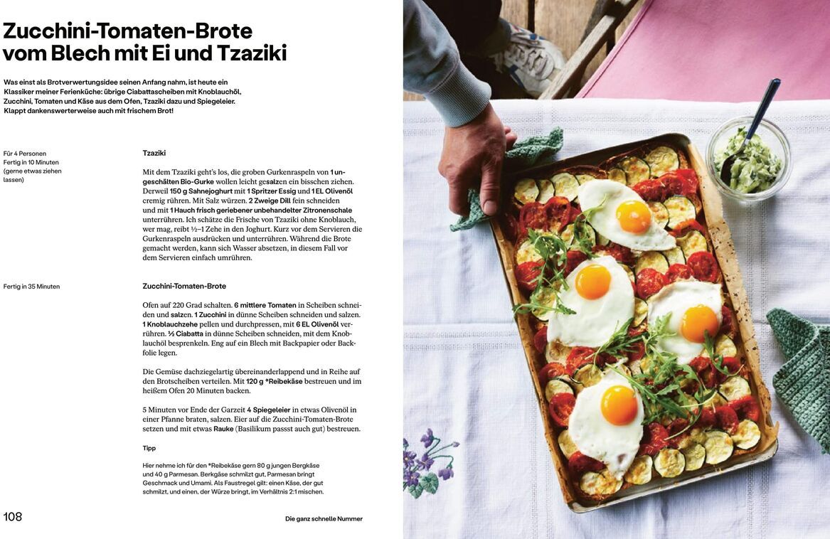 Ein aufgeschlagenes Kochbuch mit dem Titel 'Paul, Stevan: Einfach Urlaub' zeigt ein Rezept für Zucchini-Tomaten-Brote mit Ei und Tzatziki. Ein Backblech mit diesem Gericht liegt auf einem mit einer Tischdecke bedeckten Tisch. Eine Hand hält das Blech, und daneben steht eine Schüssel mit Tzatziki. Die Farben der Zutaten sind grün, rot, weiß und gelb.