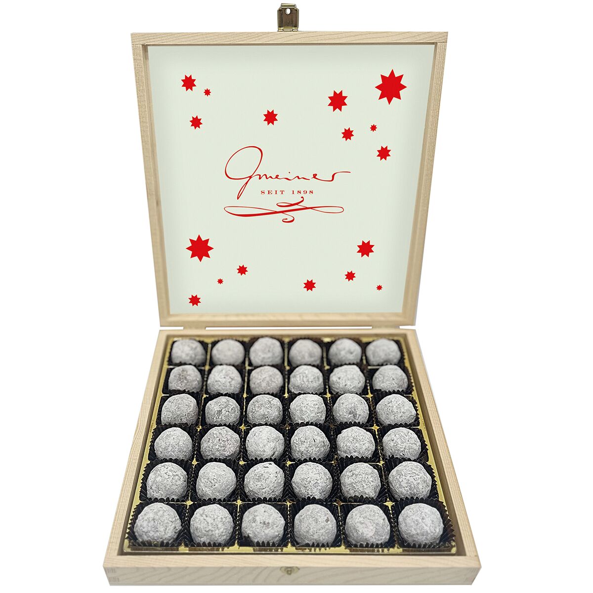Offene, elegante Holzbox mit 36 Stück champagnerverfeinerten Trüffelpralinen von Gmeiner. Die Pralinen liegen in schwarzen Papierkapseln auf goldener Einlage. Der Deckel ist mit roten Sternen und Gmeiner-Schriftzug verziert. Edler, luxuriöser Gesamteindruck.