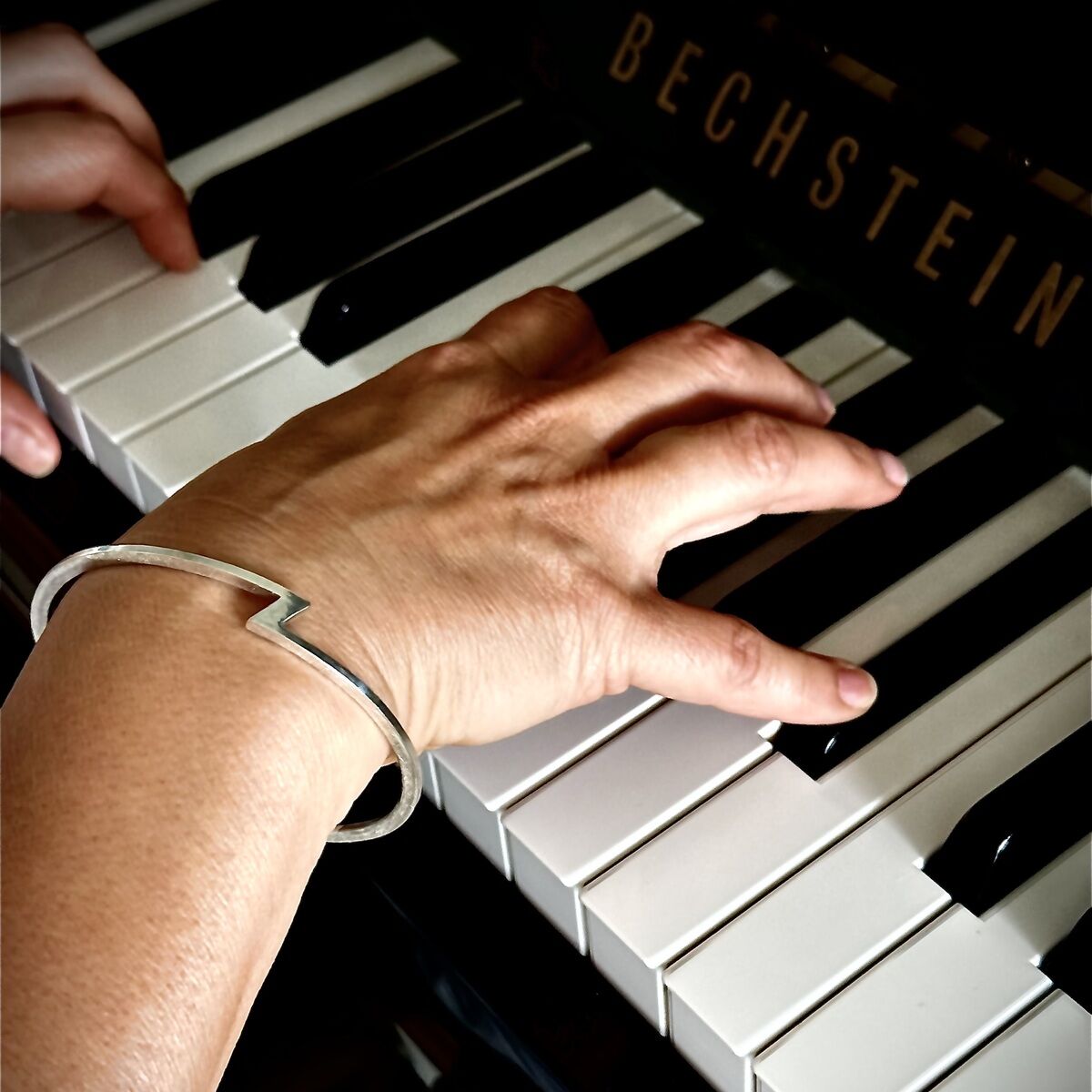 Eine Hand spielt auf einem schwarz-weißen Klavier von Bechstein. Am Handgelenk trägt die Person einen eleganten, silbernen Armreif aus der ZEIT-Sonderedition von HML Berlin mit markantem Z-Design. Die Szene wirkt edel, modern und detailreich beleuchtet.