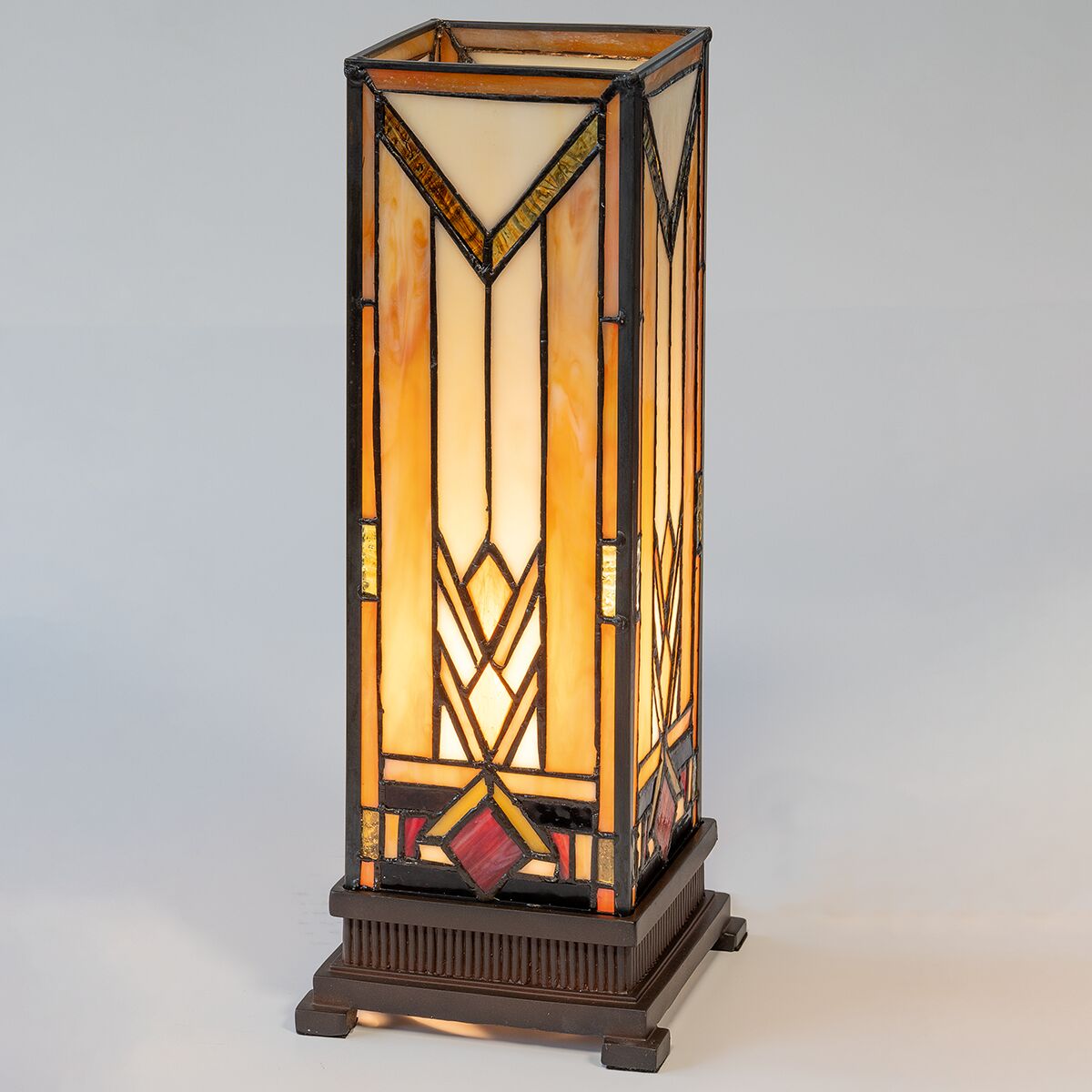 Rechteckige Tischleuchte "Soirée" von Ars mundi im Stil von Louis C. Tiffany. Der Glas-Lampenschirm mit geometrischem Jugendstil-Muster aus Elfenbein, Bernstein und weinroten Tönen sitzt auf einem massiven braunen Resinsockel. Die Leuchte verströmt warmes Licht.