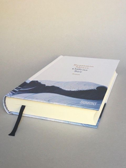 Ein Buch mit dem Titel 'Offene See' von Benjamin Myers, veröffentlicht von Dumont, liegt auf einer Oberfläche. Das Cover zeigt eine Meereslandschaft in Blau- und Grautönen.