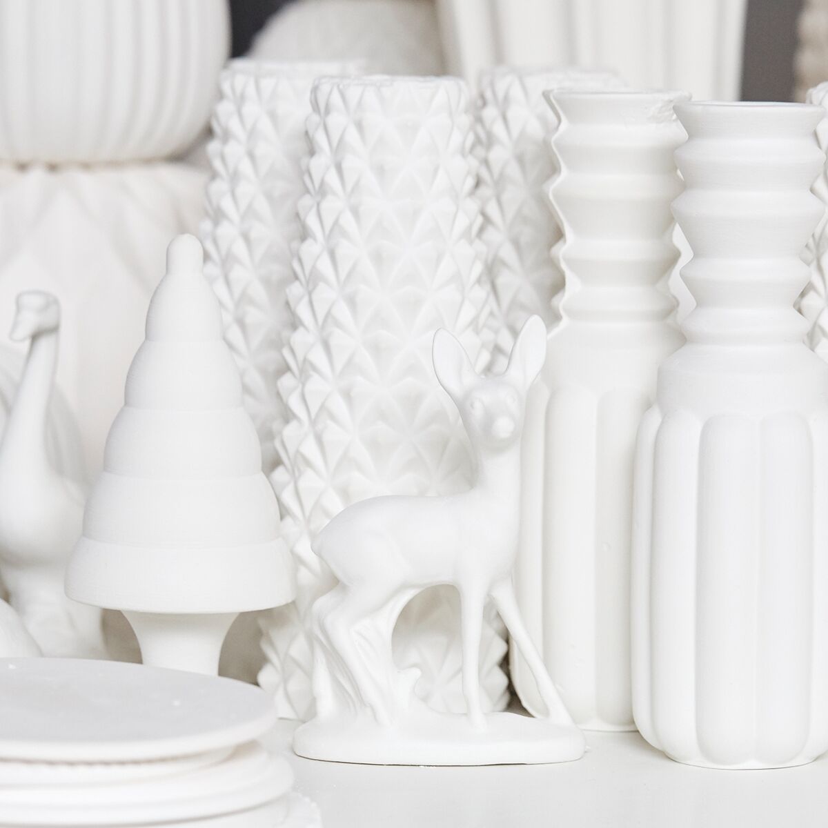 Eine detailreiche Porzellanfigur eines stehenden Bambis steht vor zwei stilisierten Tannenbäumen, umgeben von weiteren weißen Porzellanelementen. Die Szene wirkt modern und winterlich, perfekt als skandinavische Weihnachtsdekoration oder als edler Tischschmuck im Advent.