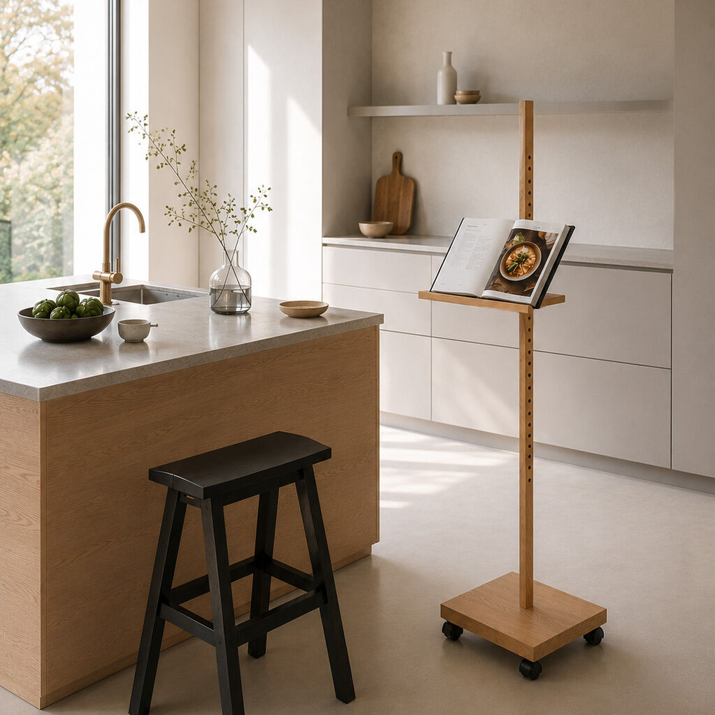 Helle, moderne Küche mit Kochinsel aus Holz, darauf eine Vase mit Zweigen. Rechts steht das mobile Device-Stativ »ERA« von Frau Caze aus Eiche mit Rollen, höhenverstellbar, darauf offen ein Kochbuch. Dezente, ruhige Farbgestaltung, viel Tageslicht, stilvoll und aufgeräumt.