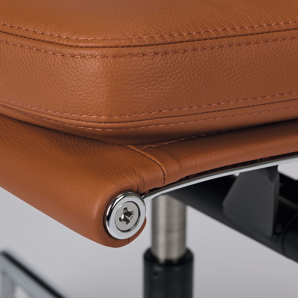 Nahaufnahme eines Vitra Soft Pad EA217 Bürostuhls in braunem Leder. Der Stuhl zeigt hochwertige Verarbeitung mit sichtbaren Nähten und einem verchromten Drehgelenk.