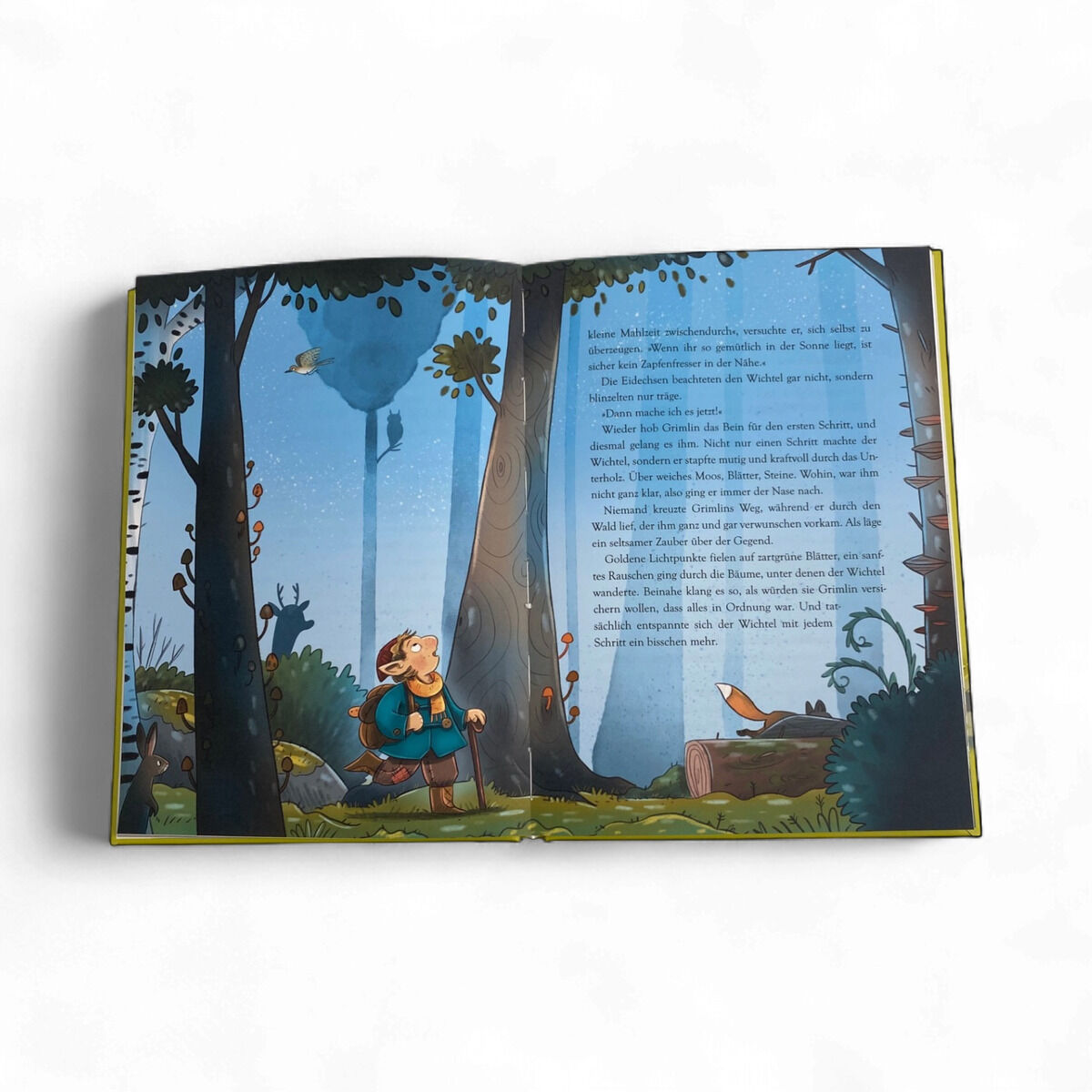 Das geöffnete Kinderbuch "Der kleine Grimlin und die große Portion Mut" zeigt eine farbenfrohe Illustrations-Doppelseite: Links wandert ein kleiner Wichtel mit Rucksack durch einen blaugrünen, märchenhaften Wald, rechts ein großer blauer Textblock zwischen Bäumen. Umgeben von freundlichen Tieren und dichter Vegetation.