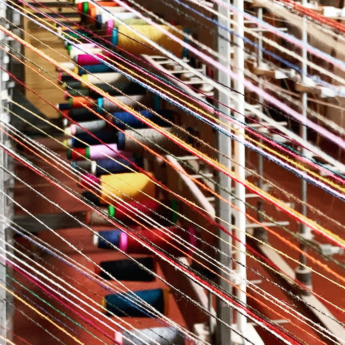 Nahaufnahme eines Webstuhls mit verschiedenen bunten Fäden in den Farben rot, gelb, blau, grün, rosa, violett, weiß, braun, grau und schwarz.